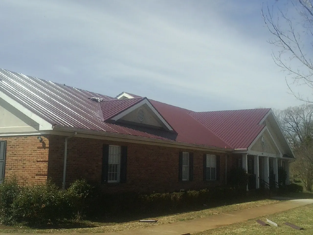 Red metal roof with gabled entries on a long brick building, from a Hail Damage Roof Repair job in Haydenville