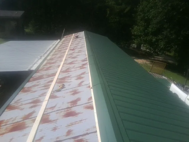 Old rusted panels beside newly installed green metal roofing — Wind Damage Roof Repair by Roofing Brothers in Haydenville