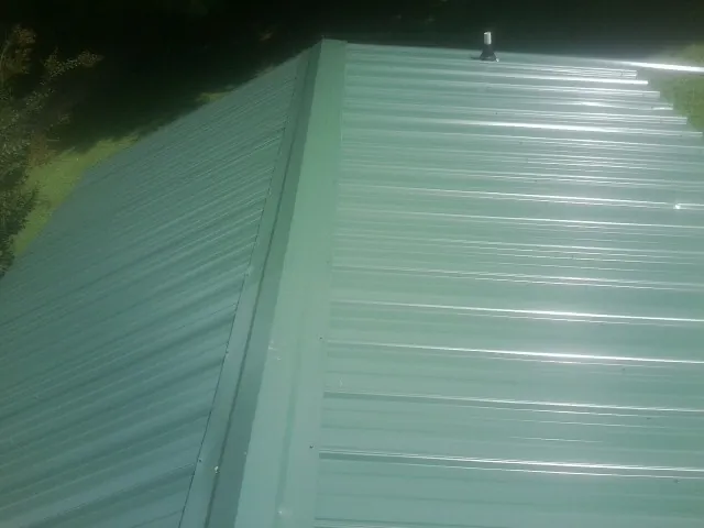 New green metal panels meeting at the ridge of a roof — Flat Roof Repair work by our crew in Haydenville