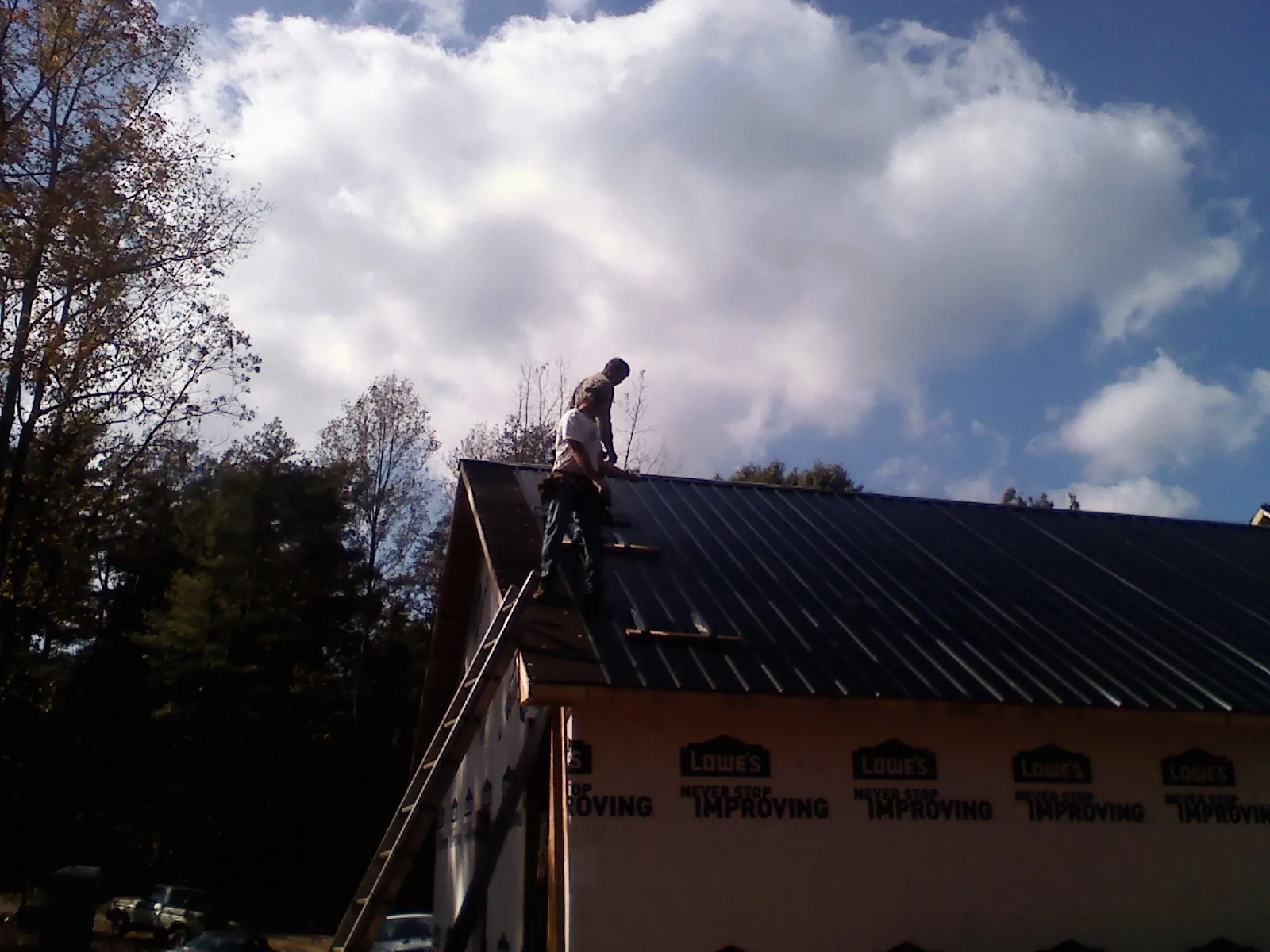 Roofer fastening dark metal panels high against a cloudy sky, from a Roof Inspection job in Haydenville