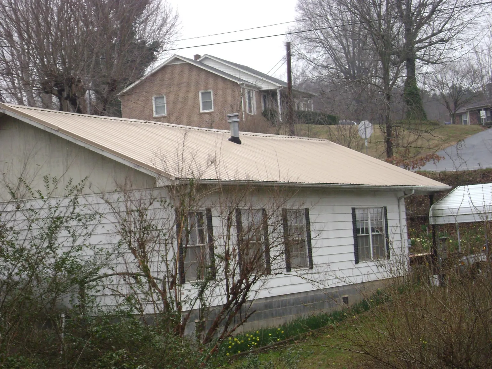 Tan metal roof on a white sided house set into a hillside — Commercial Roofing by Roofing Brothers in Haydenville